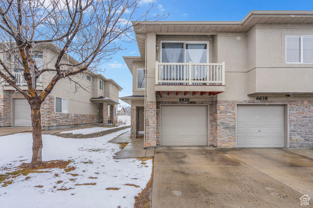 View of property featuring a garage, concrete driveway, a balcony, and stucco siding