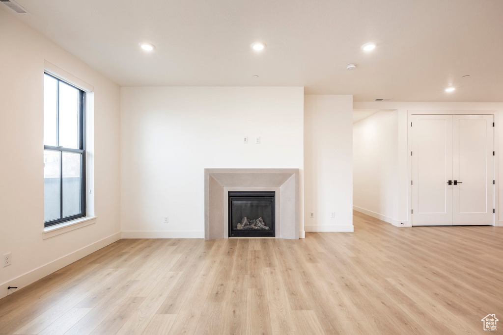 Unfurnished living room featuring baseboards, a glass covered fireplace, light wood-style flooring, and recessed lighting