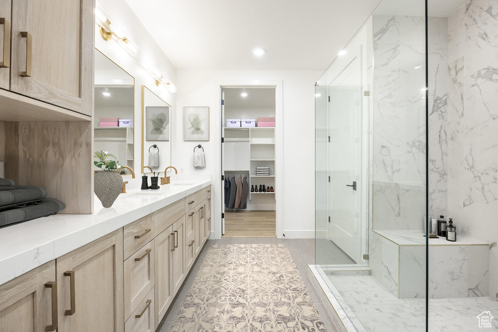 Bathroom featuring a sink, a spacious closet, a marble finish shower, and double vanity