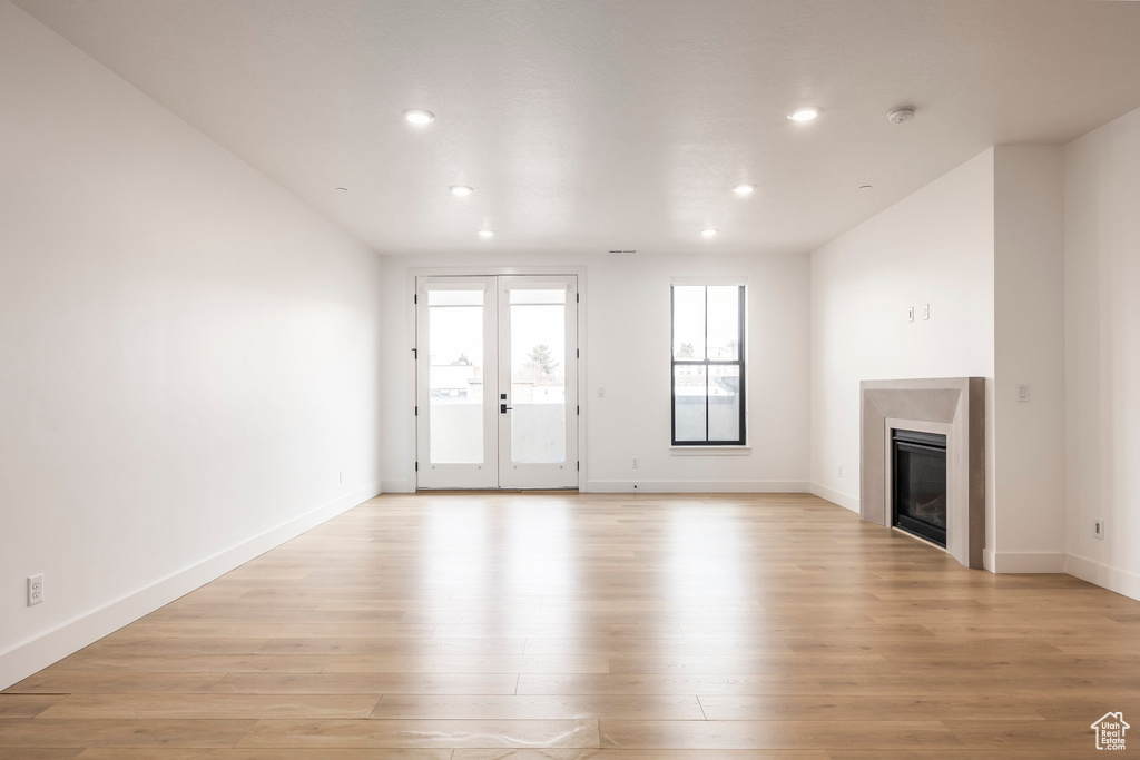 Unfurnished living room featuring french doors, recessed lighting, a glass covered fireplace, light wood-type flooring, and baseboards