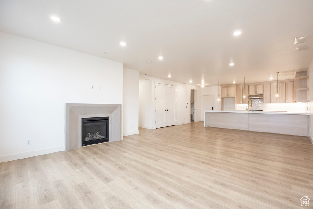 Unfurnished living room with a fireplace, light wood finished floors, recessed lighting, a sink, and baseboards