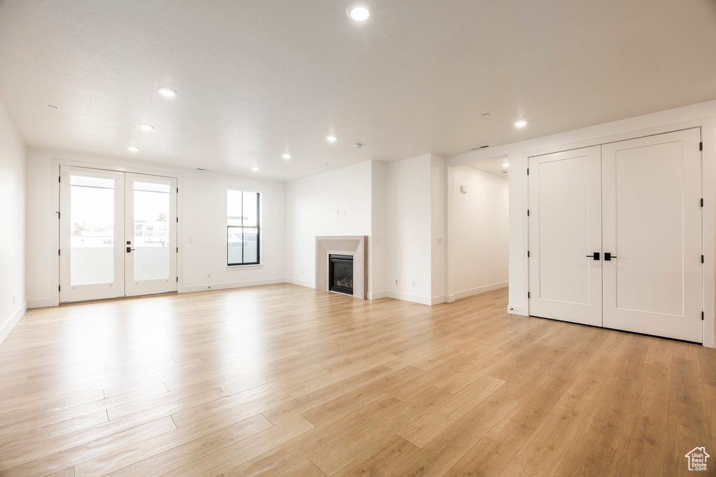 Unfurnished living room featuring french doors, a glass covered fireplace, light wood-style flooring, and recessed lighting