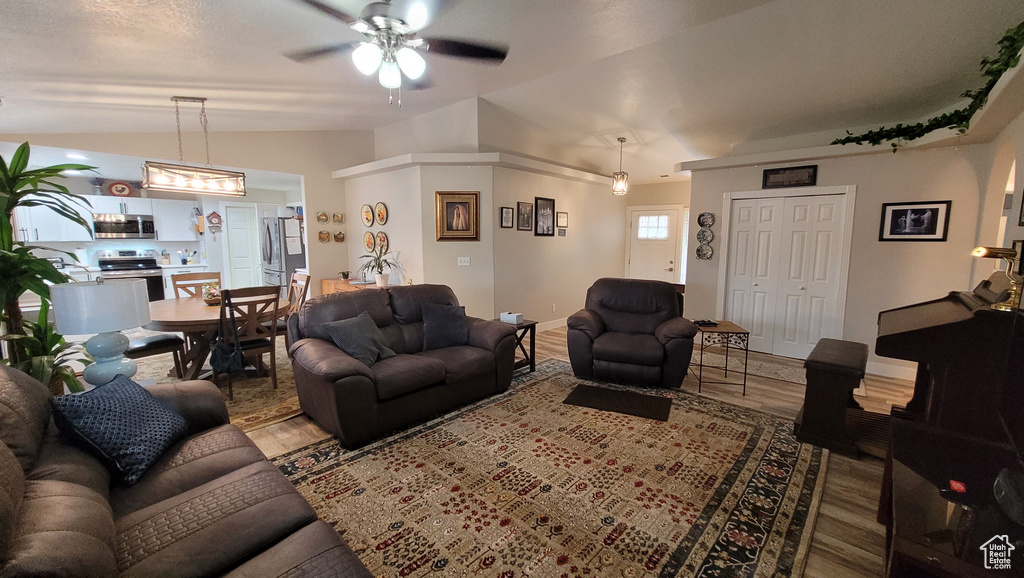 Living area featuring a ceiling fan, lofted ceiling, baseboards, and wood finished floors