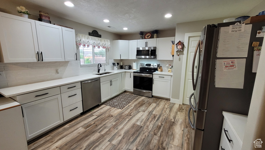 Kitchen featuring white cabinets, stainless steel appliances, light countertops, light wood-style floors, and a sink