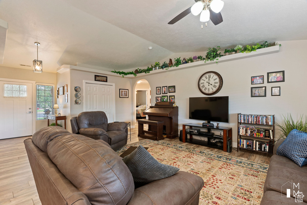 Living room featuring light wood-style flooring, arched walkways, vaulted ceiling, and a ceiling fan