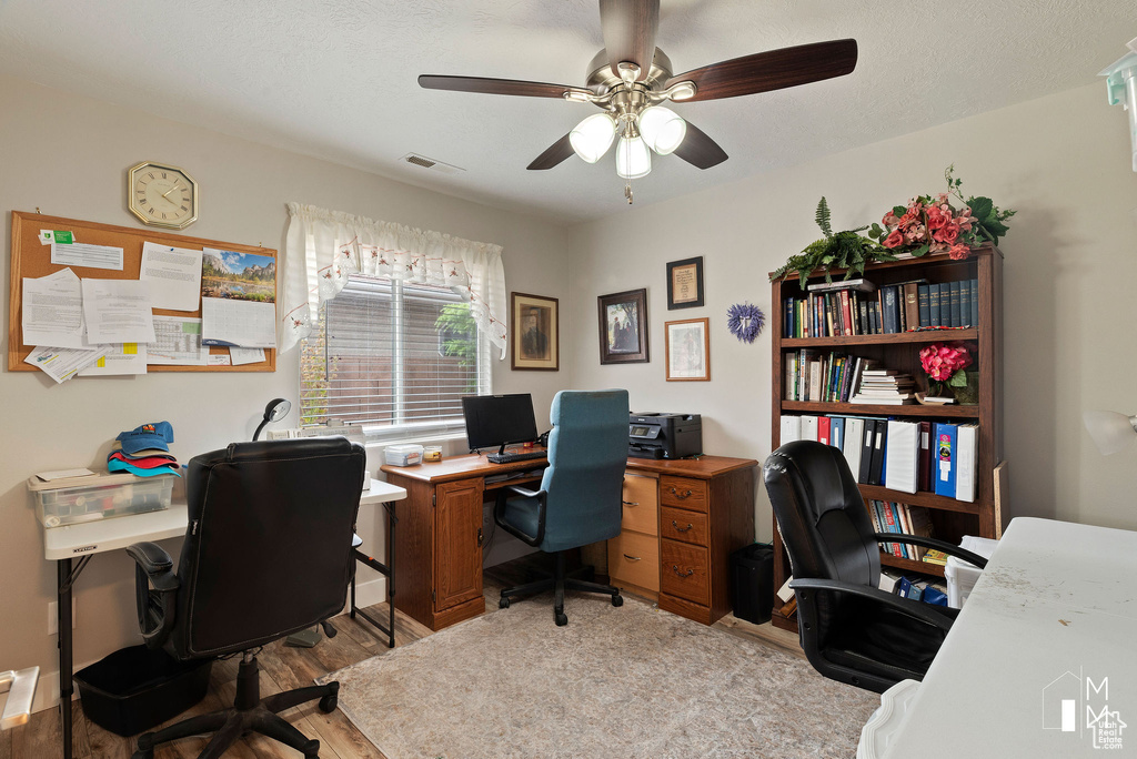 Office area featuring light wood-style flooring, visible vents, ceiling fan, and a textured ceiling