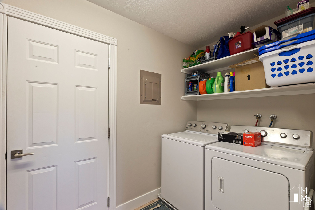 Clothes washing area featuring laundry area, electric panel, baseboards, washer and dryer, and a textured ceiling