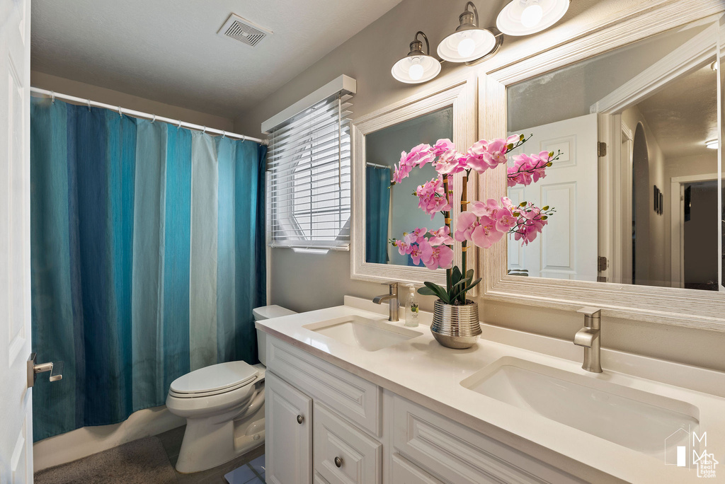 Full bath featuring double vanity, visible vents, toilet, and a sink