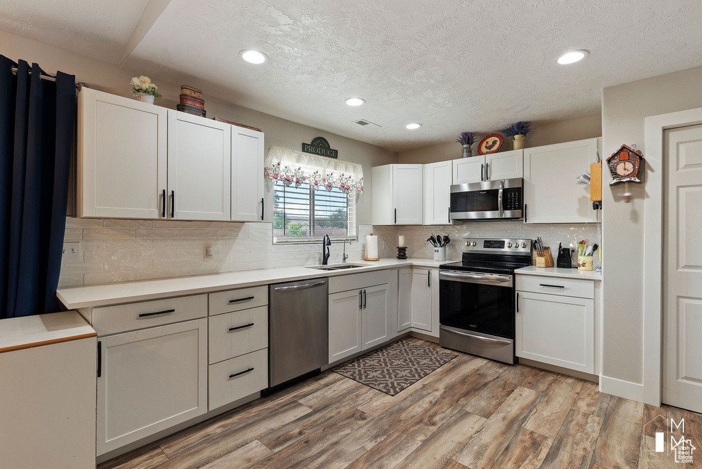 Kitchen with light wood finished floors, white cabinets, appliances with stainless steel finishes, light countertops, and a sink