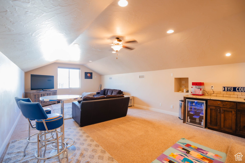Living area featuring beverage cooler, light carpet, baseboards, vaulted ceiling, and a bar