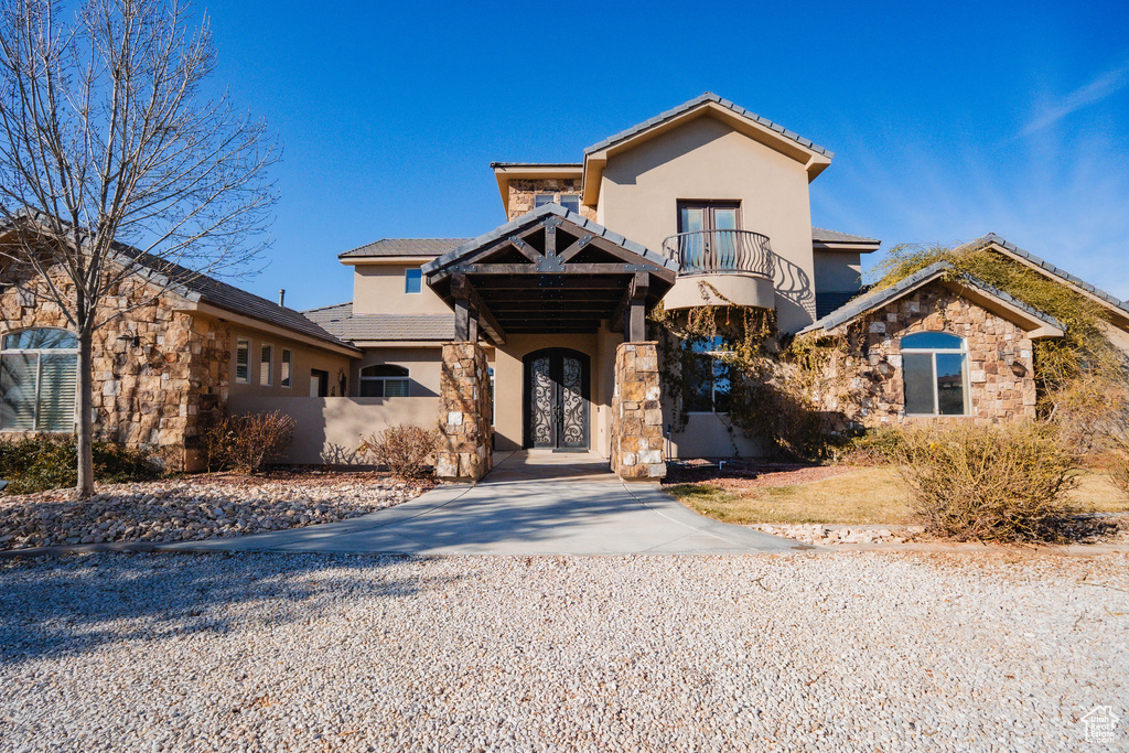 Mediterranean / spanish-style house featuring stucco siding, a balcony, stone siding, driveway, and a tiled roof