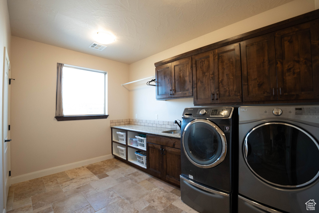 Laundry area with washing machine and dryer, a sink, visible vents, baseboards, and cabinet space