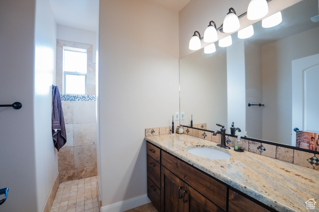 Full bath with baseboards, tiled shower, and vanity