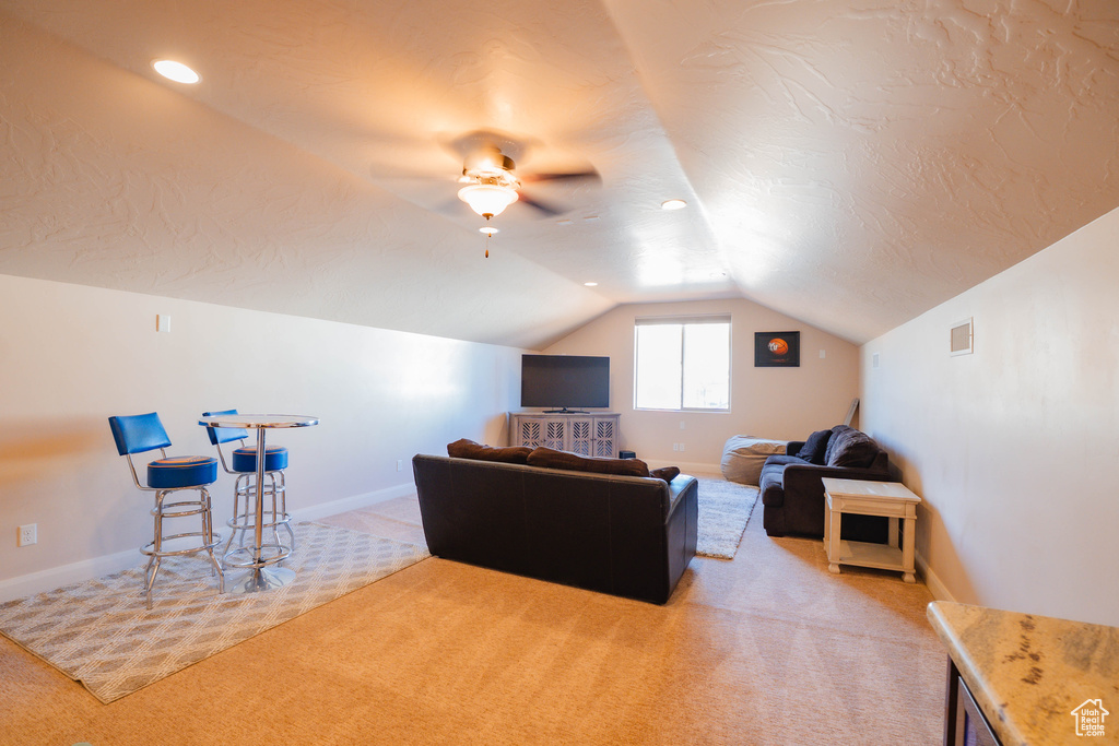 Living area with light carpet, vaulted ceiling, visible vents, and baseboards