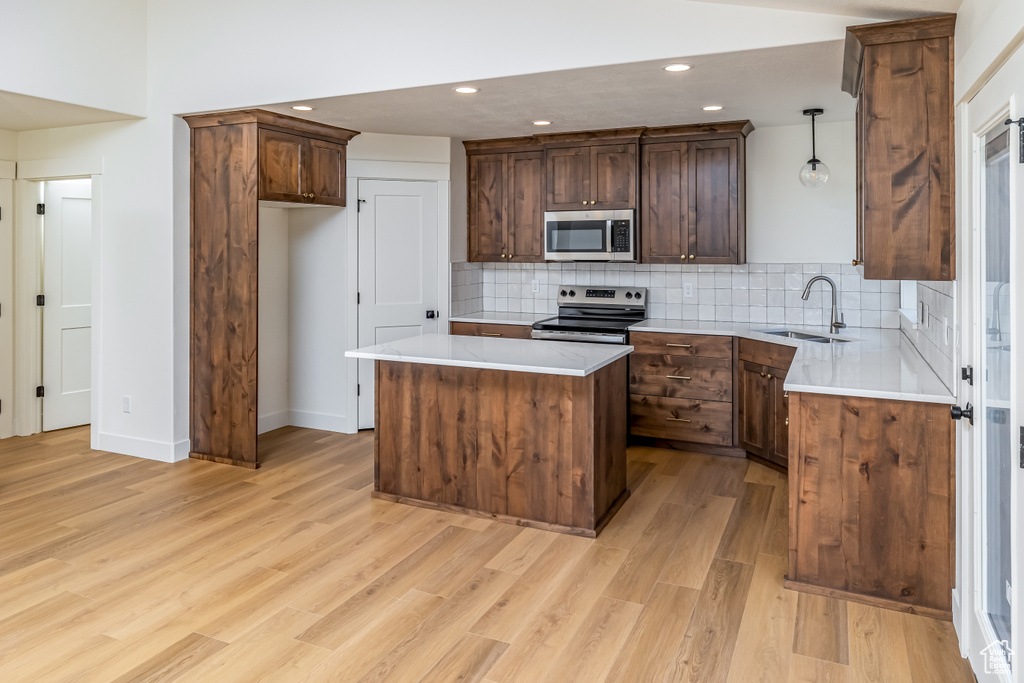 Kitchen featuring light wood-style flooring, stainless steel appliances, a kitchen island, light countertops, and decorative light fixtures