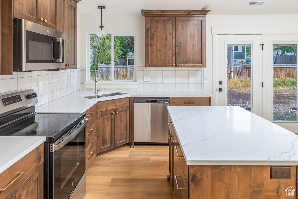 Kitchen with appliances with stainless steel finishes, decorative light fixtures, a sink, light wood-style floors, and backsplash