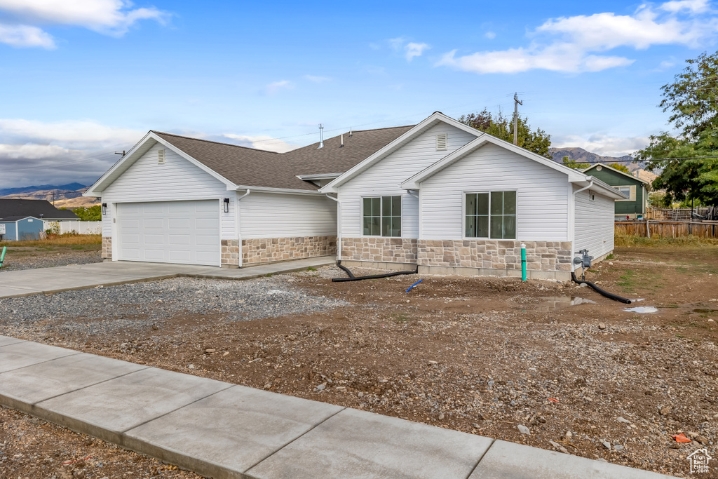 Ranch-style home featuring an attached garage, a mountain view, a shingled roof, driveway, and stone siding