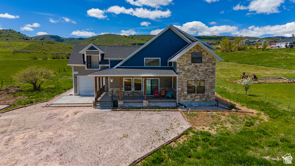 Exterior space with driveway, a shingled roof, stone siding, a mountain view, and a porch