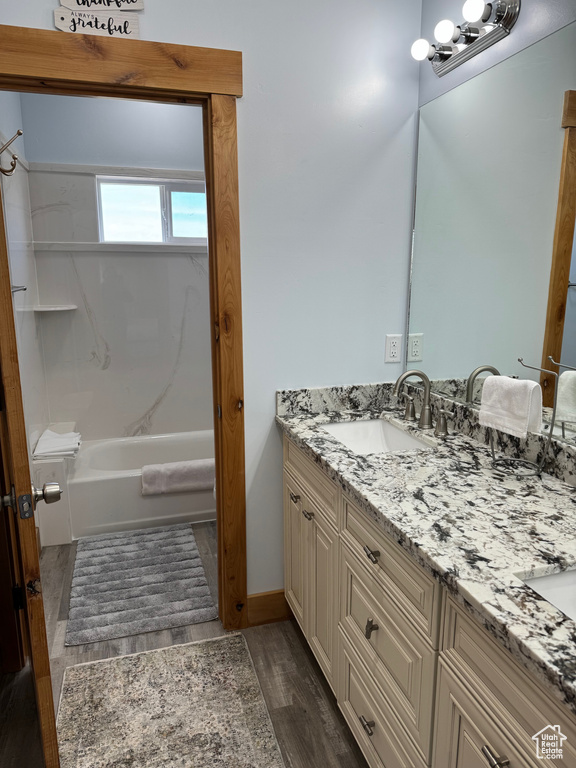 Bathroom featuring double vanity, wood finished floors, tub / shower combination, and a sink