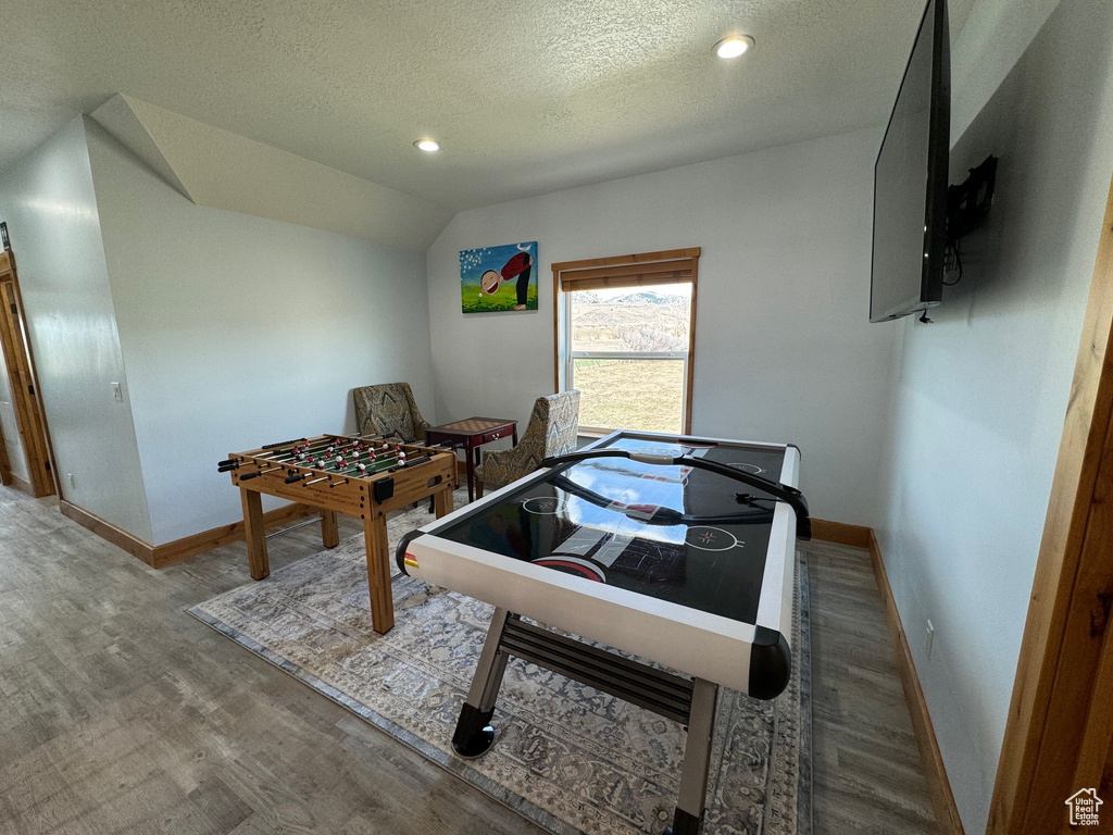 Rec room featuring lofted ceiling, a textured ceiling, wood finished floors, and baseboards