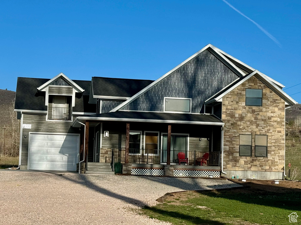 View of front of home featuring driveway, stone siding, an attached garage, covered porch, and crawl space