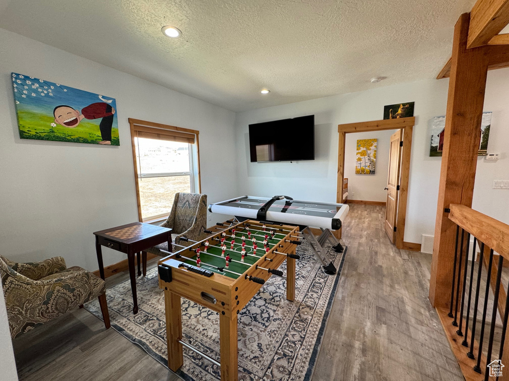 Recreation room with a textured ceiling, baseboards, wood finished floors, and recessed lighting