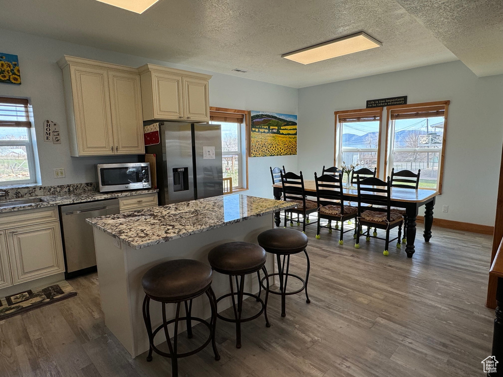 Kitchen with light stone counters, stainless steel appliances, a kitchen island, wood finished floors, and plenty of natural light