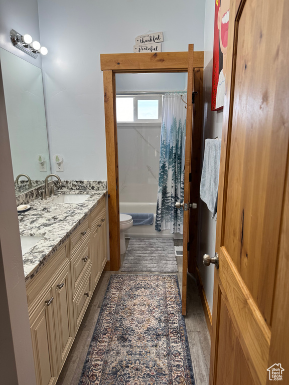 Full bathroom featuring double vanity, toilet, shower / tub combo, a sink, and wood finished floors