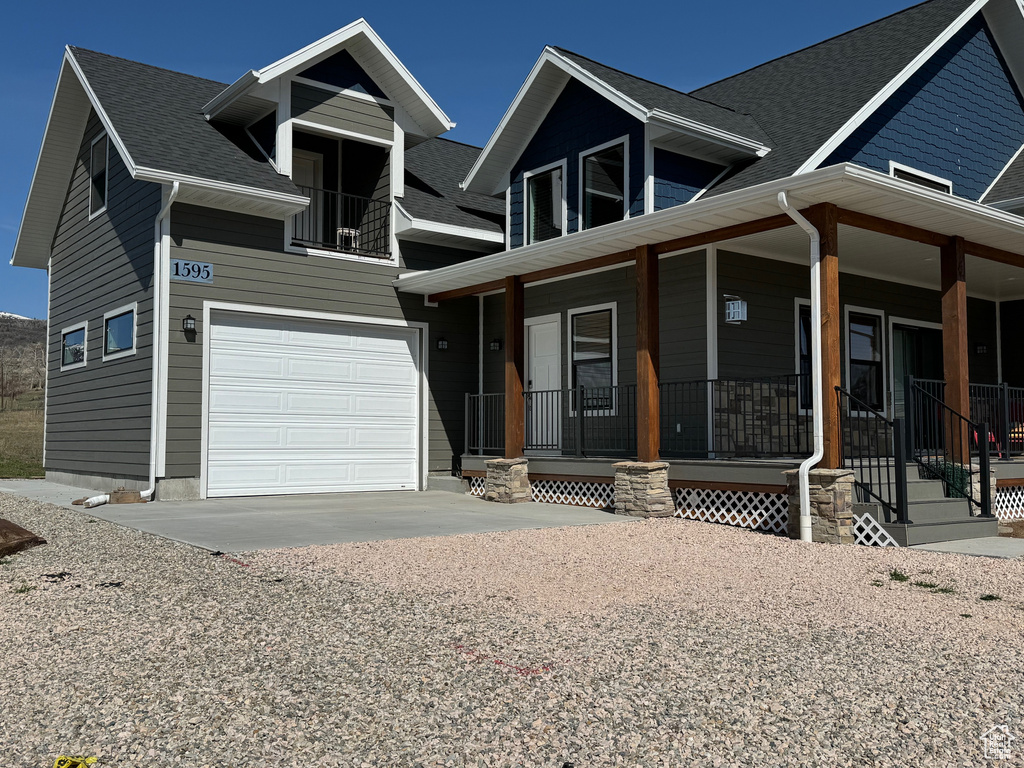 View of front facade featuring driveway, covered porch, and roof with shingles