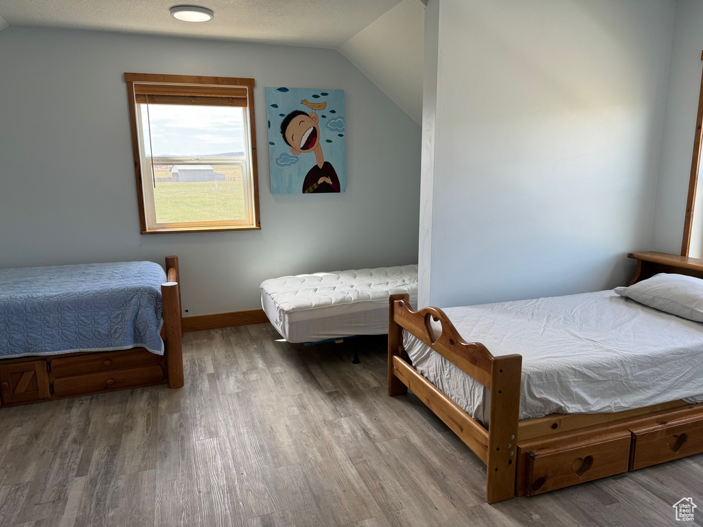 Bedroom with vaulted ceiling, wood finished floors, and baseboards