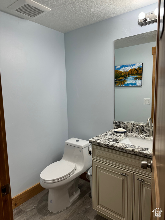 Half bathroom with visible vents, toilet, wood finished floors, a textured ceiling, and vanity