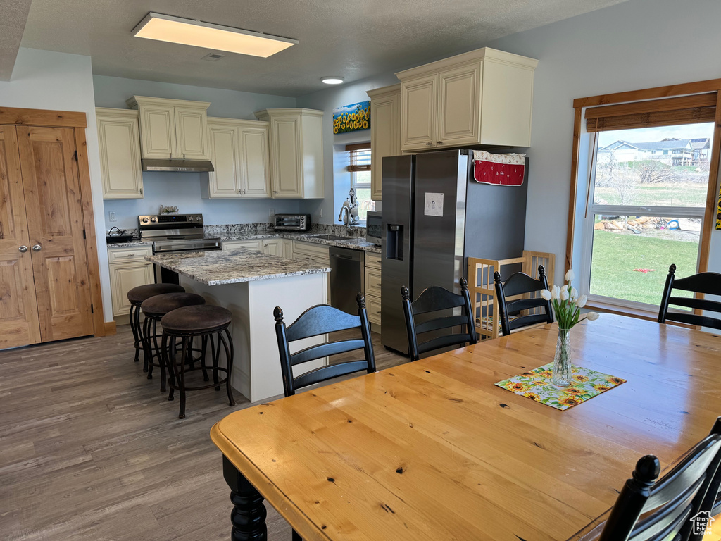 Kitchen featuring under cabinet range hood, a kitchen island, a sink, appliances with stainless steel finishes, and cream cabinetry