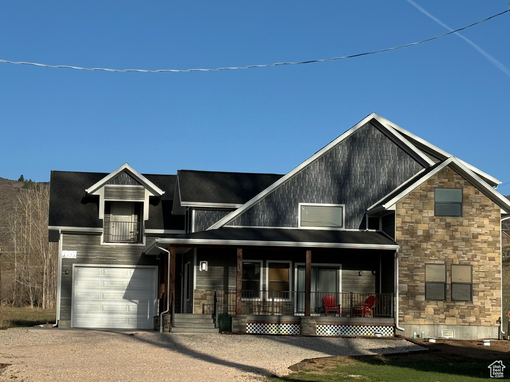 View of front of property with a garage, driveway, stone siding, crawl space, and a porch