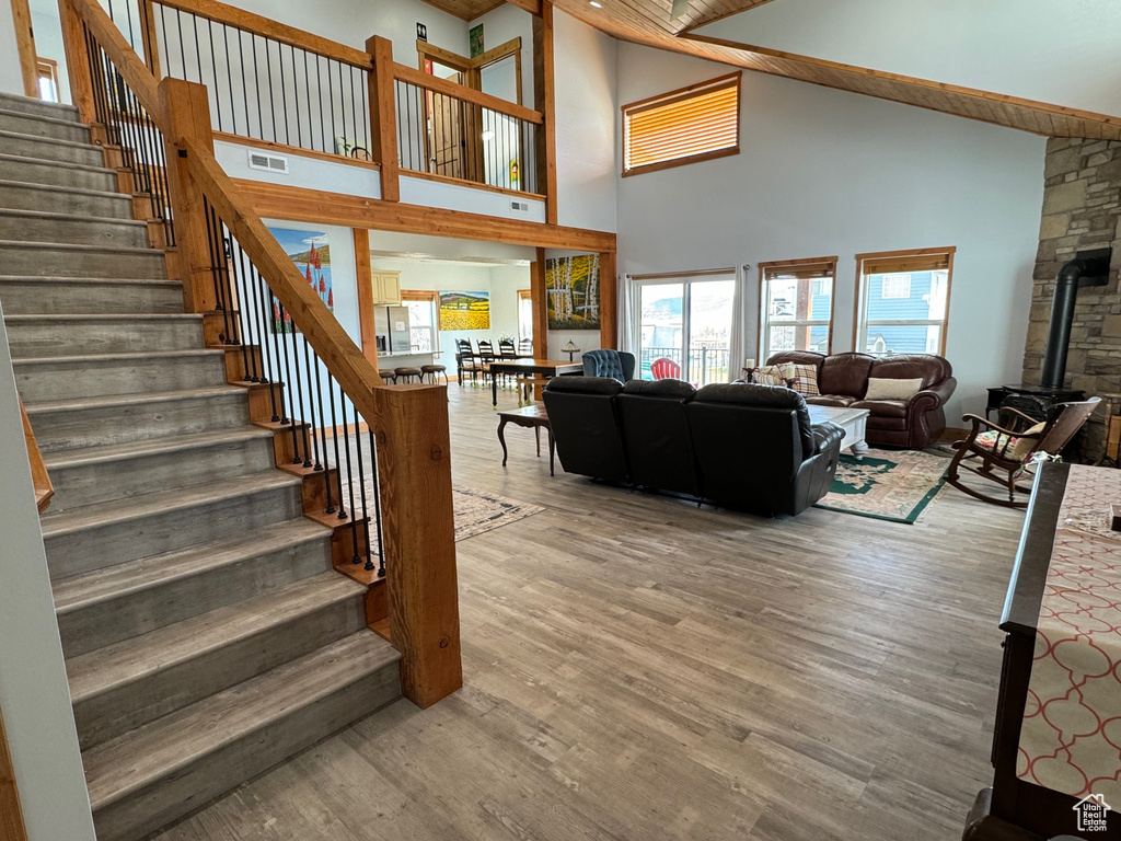 Living room with visible vents, a wood stove, wood finished floors, high vaulted ceiling, and stairs