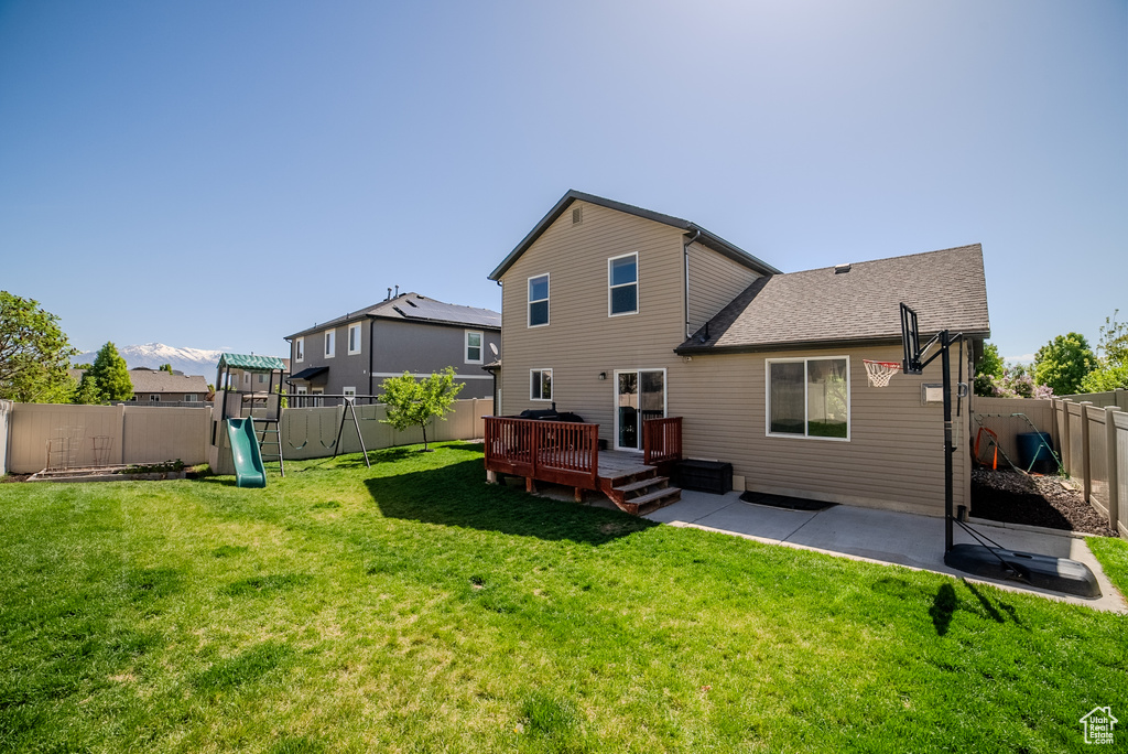 Rear view of house featuring a playground, a patio, a deck, and roof with shingles
