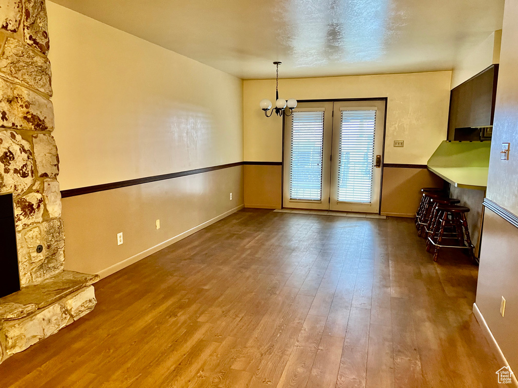 Unfurnished living room featuring baseboards, wood finished floors, and a notable chandelier