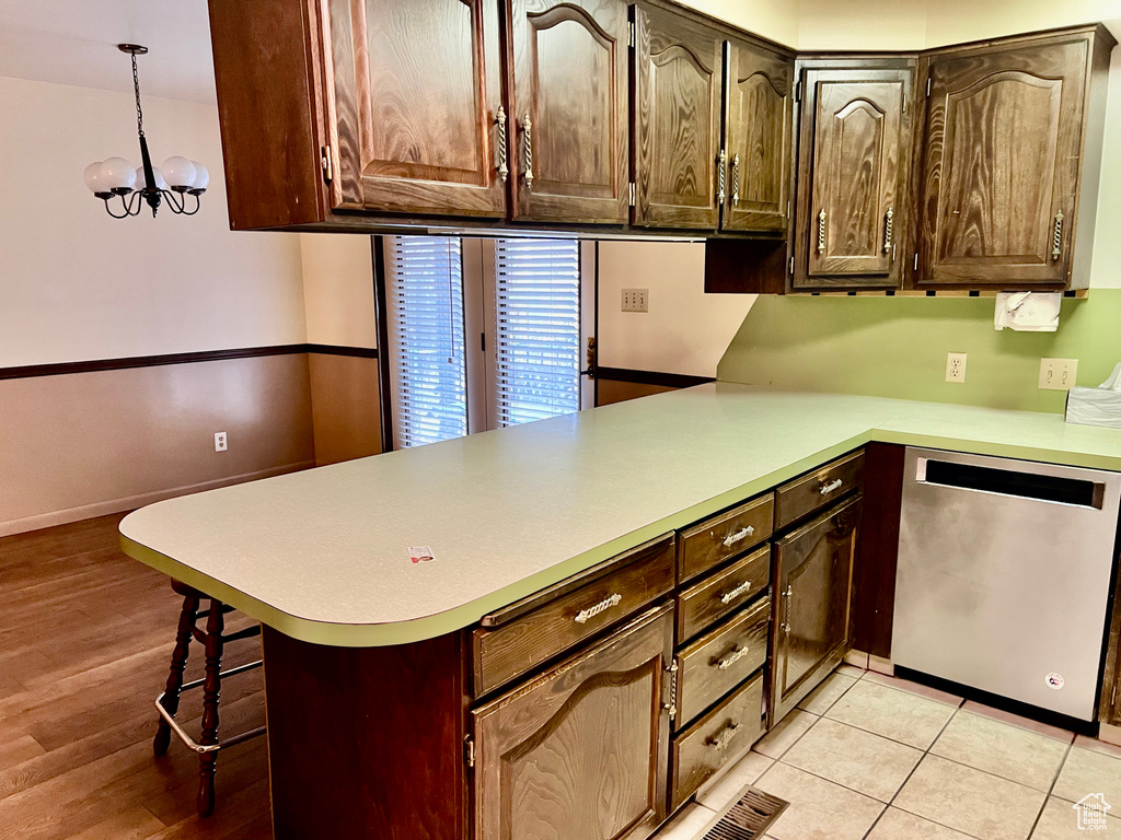 Kitchen with dishwasher, decorative light fixtures, a peninsula, light countertops, and a kitchen bar