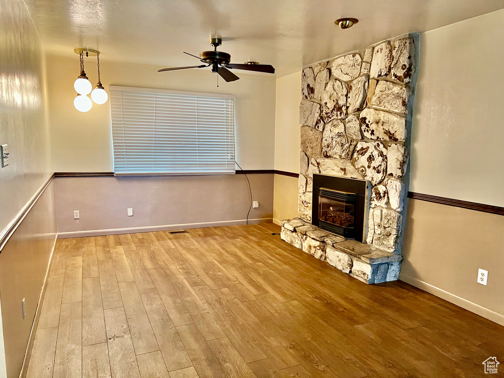 Unfurnished living room with ceiling fan, a stone fireplace, wood finished floors, and baseboards