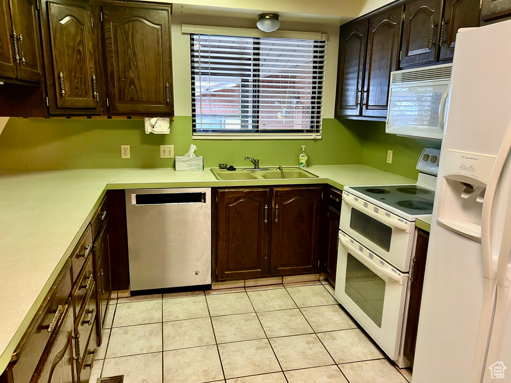Kitchen with light countertops, white appliances, a sink, and dark brown cabinetry
