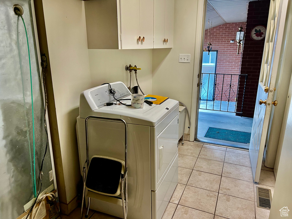 Washroom featuring washing machine and dryer, visible vents, cabinet space, and light tile patterned flooring