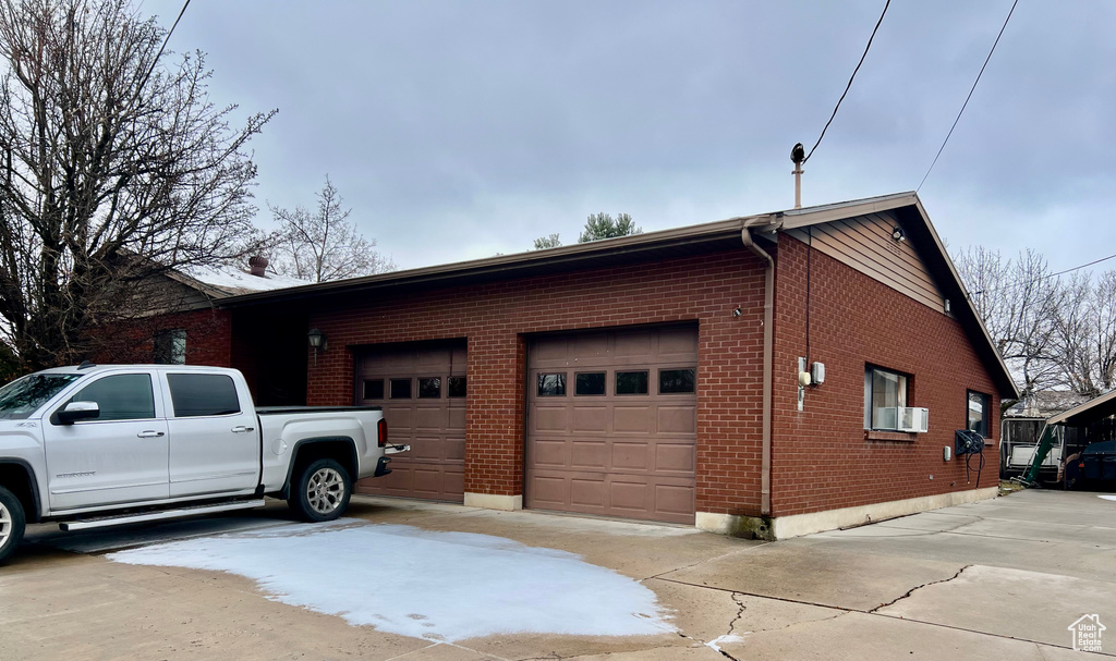 View of side of property with driveway, a garage, cooling unit, and brick siding