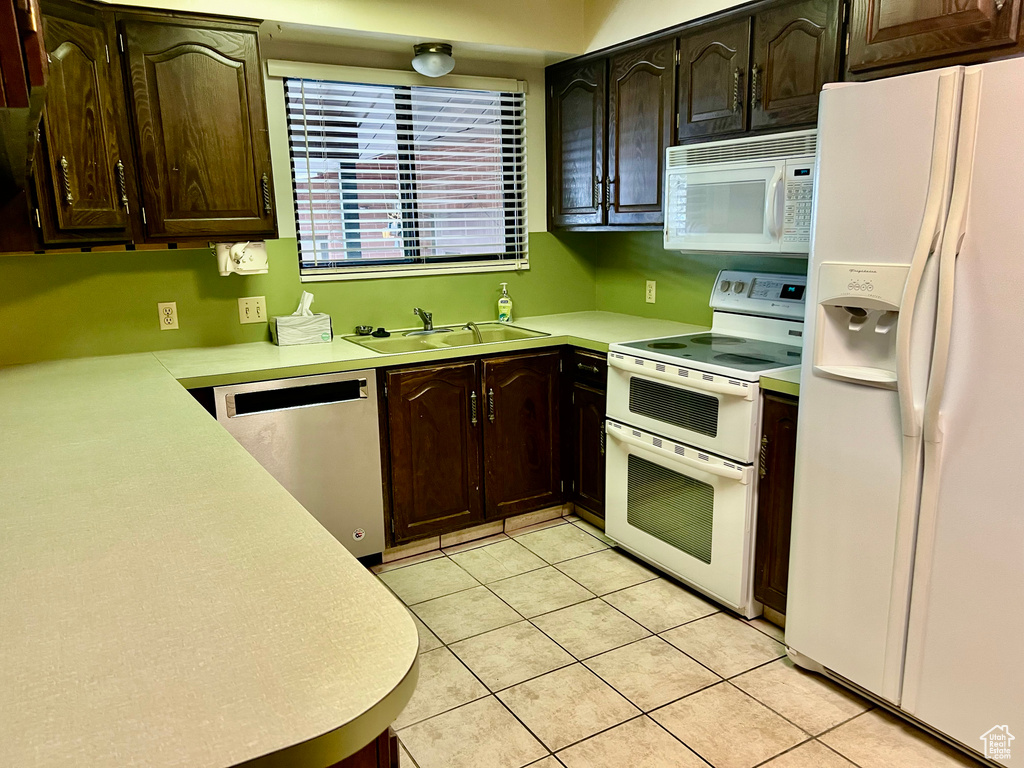 Kitchen featuring white appliances, light countertops, a sink, and dark brown cabinets