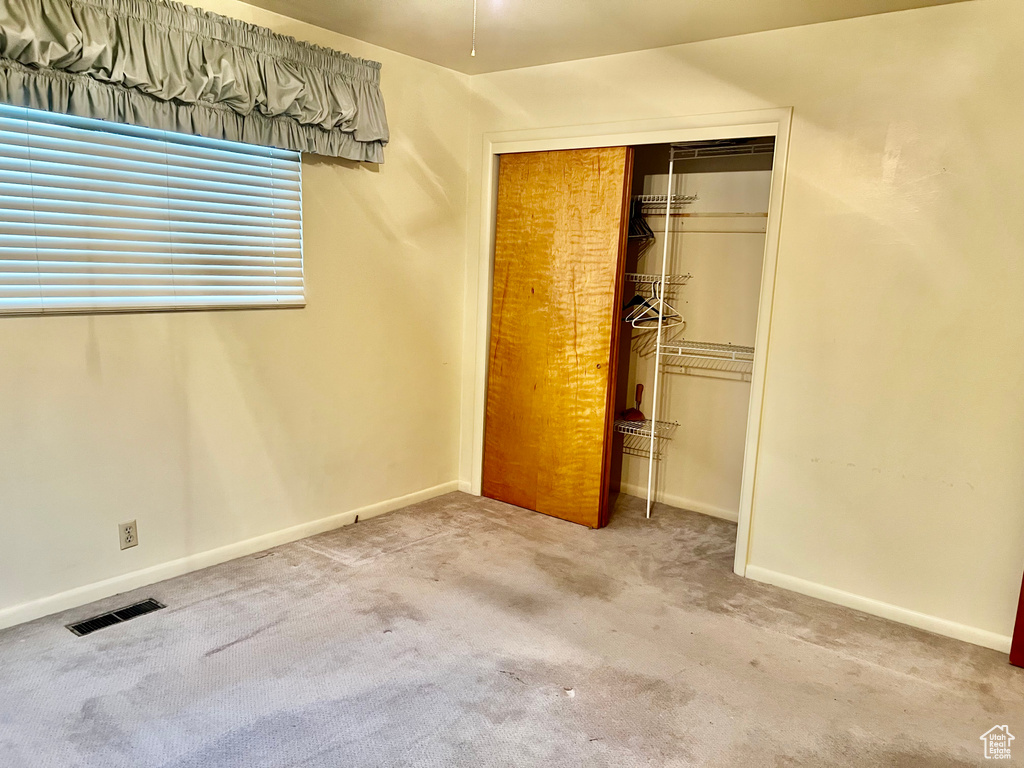 Unfurnished bedroom with light carpet, baseboards, visible vents, and a closet