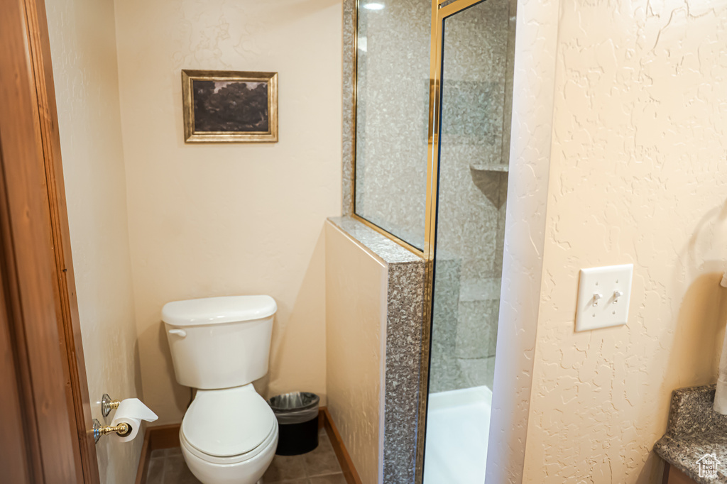 Full bath featuring a textured wall, toilet, baseboards, tile patterned floors, and a stall shower