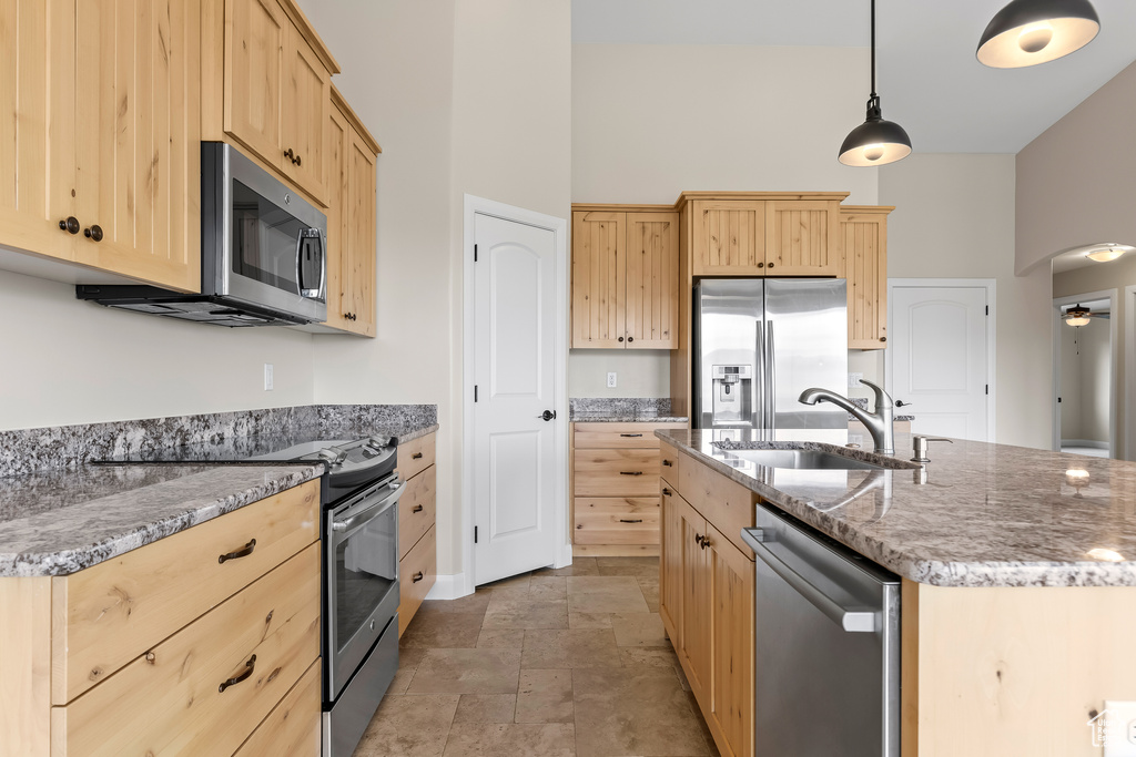 Kitchen with arched walkways, light brown cabinetry, appliances with stainless steel finishes, and a sink