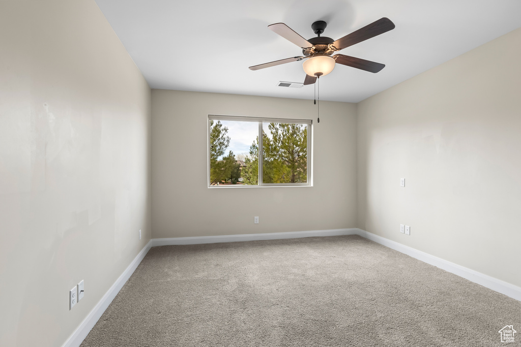 Empty room with a ceiling fan, carpet flooring, visible vents, and baseboards