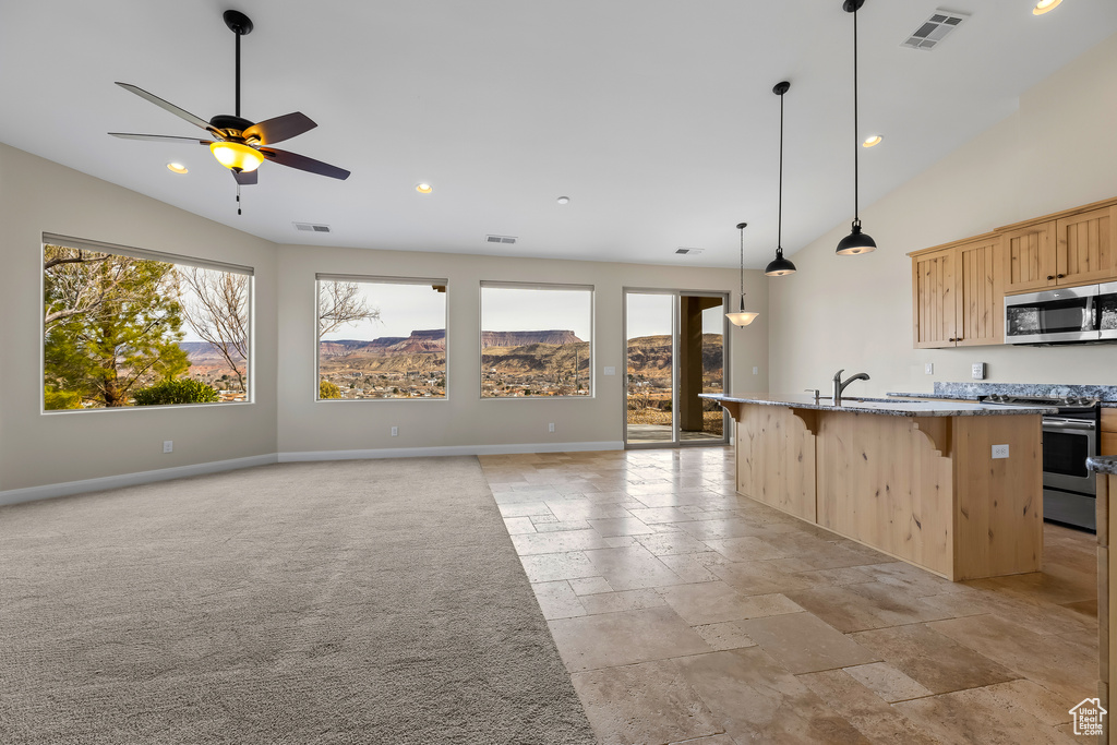 Kitchen featuring light brown cabinets, visible vents, appliances with stainless steel finishes, light stone countertops, and an island with sink