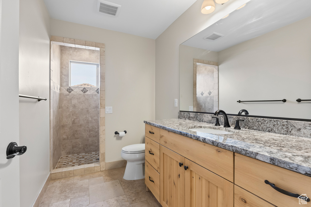 Full bath with visible vents, toilet, vanity, tiled shower, and baseboards