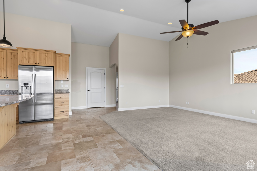 Kitchen featuring light brown cabinetry, open floor plan, stainless steel refrigerator with ice dispenser, and light stone countertops