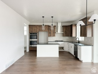 Kitchen featuring wall chimney range hood, dark countertops, appliances with stainless steel finishes, tasteful backsplash, and a kitchen island
